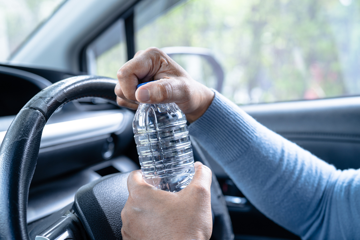 Asian woman driver holding bottle for drink water while driving a car. Plastic hot water bottle cause fire